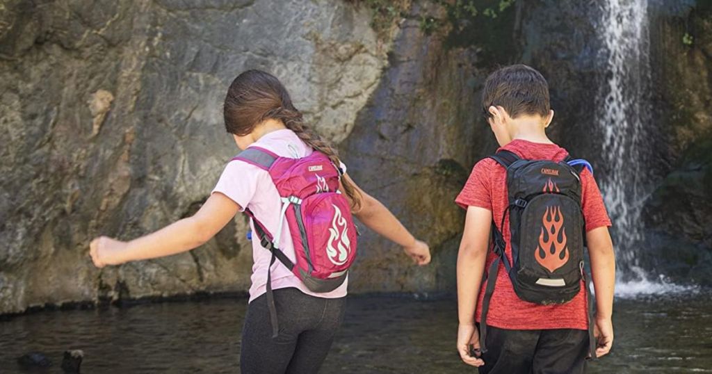 two kids wearing hydration backpacks in a natural pool with a waterfall