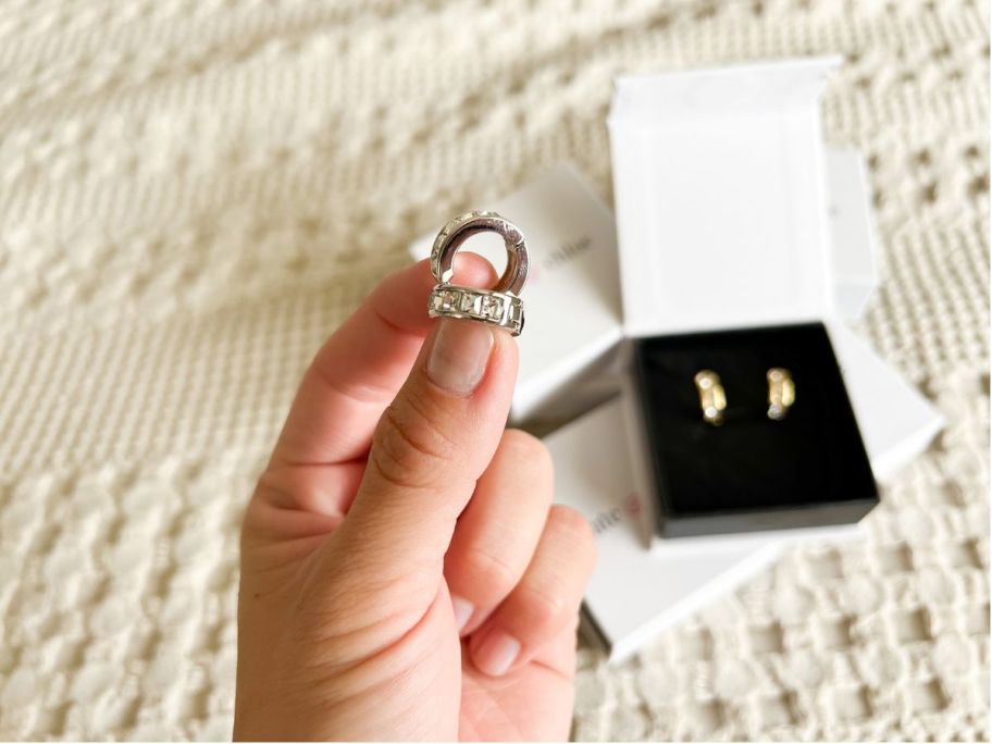 hand holding a pair of cate and chloe giselle hoop earrings between fingertips above a box with more earrings