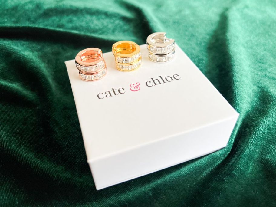 rose gold, gold, and silver Cate & Chloe Giselle Hoop Earrings sitting on top of cate & chloe jewelry box which is placed on emerald fabric