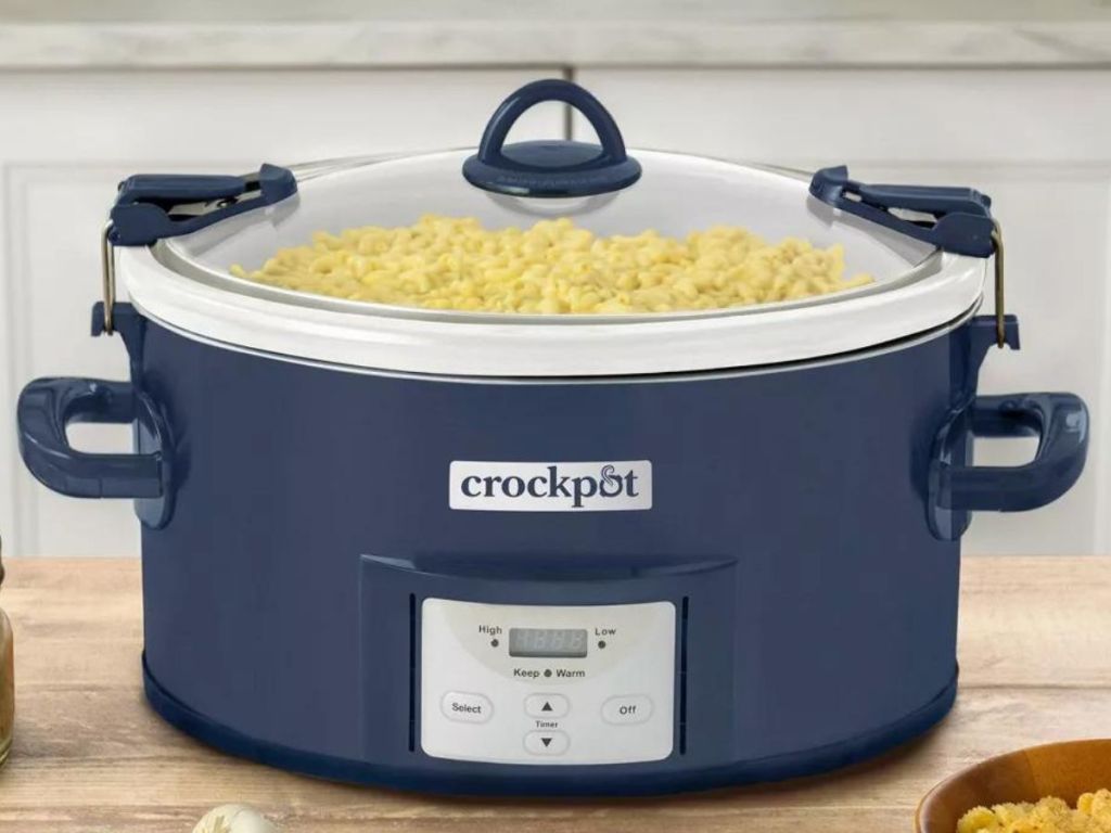 Blue slow cooker sitting on a counter with the lid on and noodles inside
