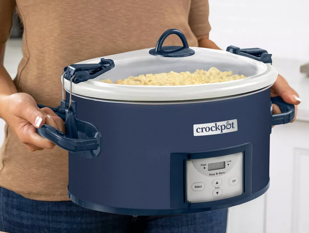 Woman carrying a blue slow cooker with the lid on.