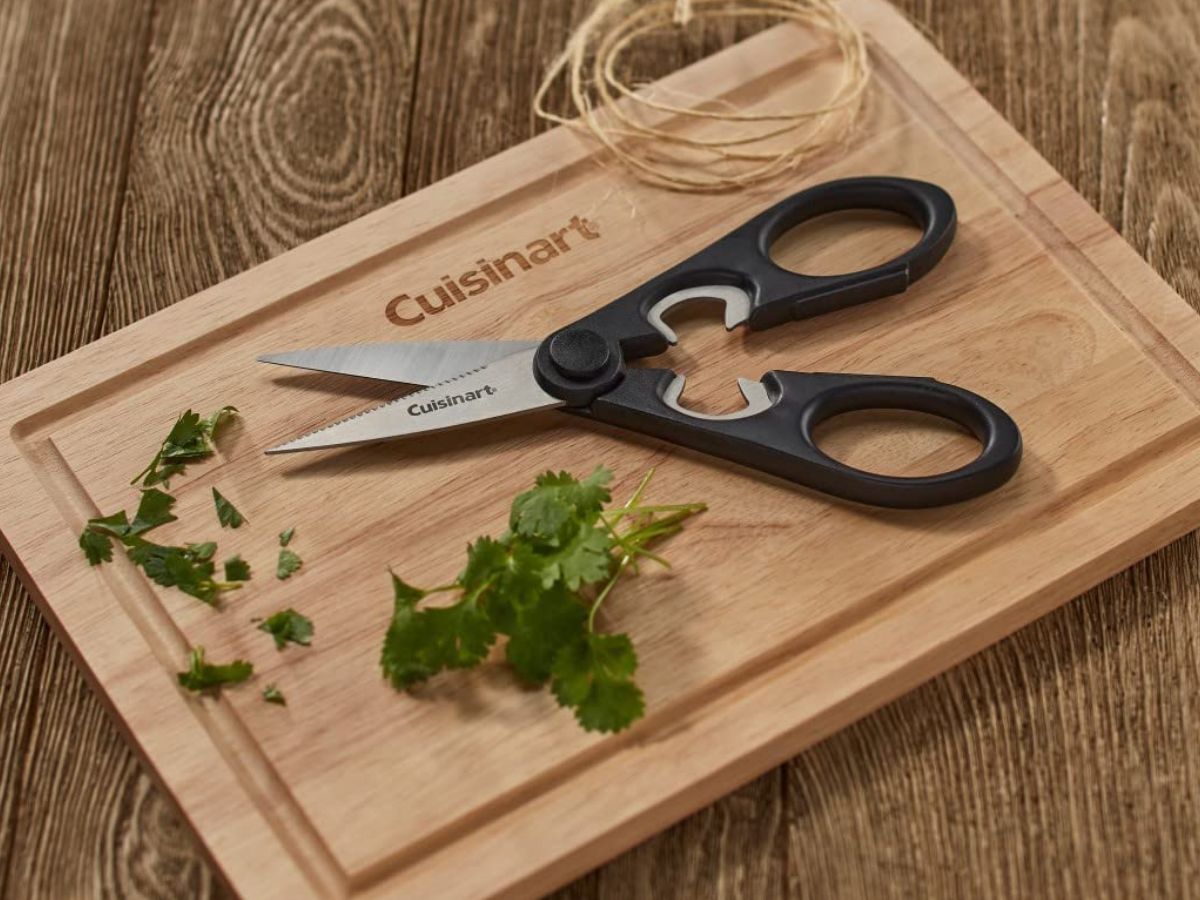 Pair of Cuisinart kitchen scissors on a cutting board with cut herbs.