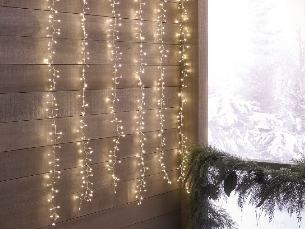 Curtain Rain String Lights displayed on a plank wall next to a large window with snow outside