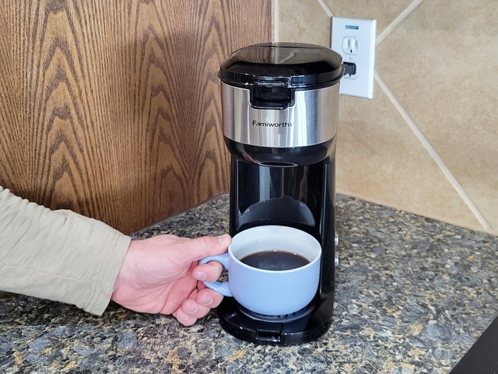 hand grabbing a cup of coffee from a single-serve coffee maker