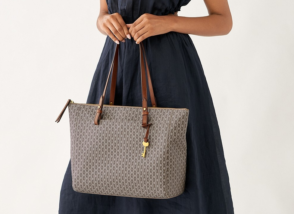 woman in a blue dress holding a Fossil tote in front of her