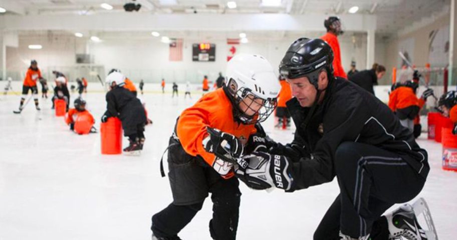 An Adult coaching a child in hockey on an ice rink