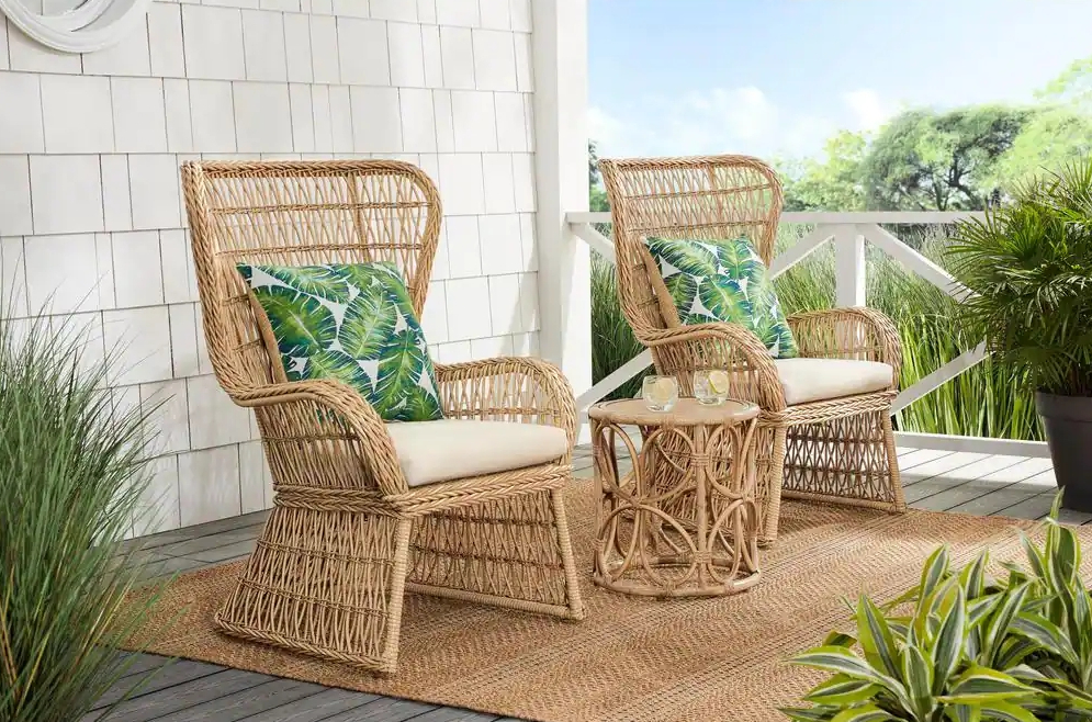 Two wicker chairs and a side table on a patio with green pillows on the chairs