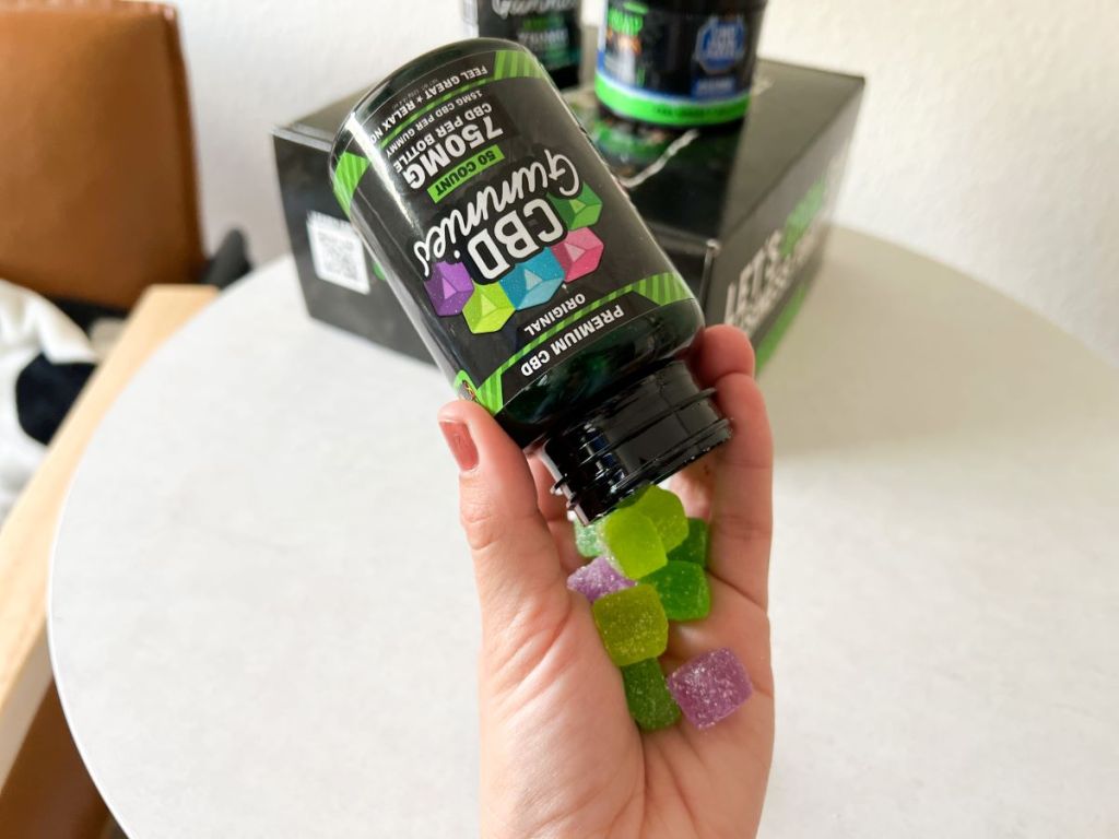 Hand holding a bottle of Hemp Bombs CBD Gummies with some of the gummies falling into the hand
