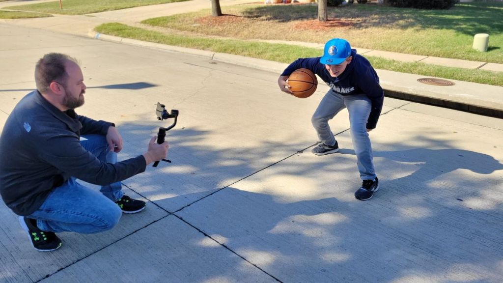 Man holding a gimbal stabilizer while filming a boy play basketball