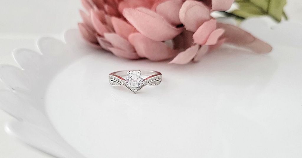 criss cross sterling silver ring on white decorate plate with pink flower behind it