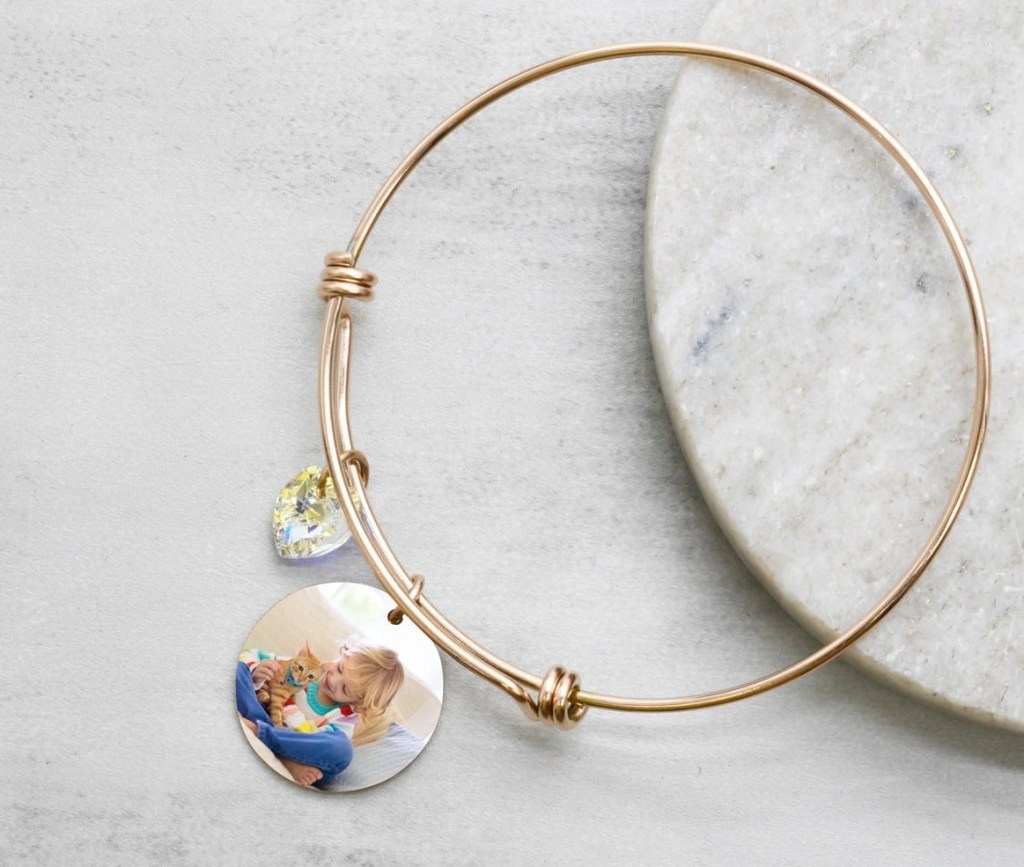 Rose gold bracelet with a charm on it that has a picture of a child and a cat