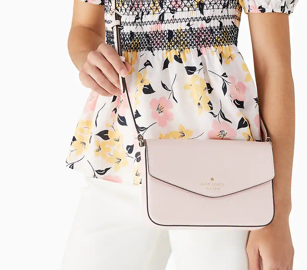 Woman in a floral shirt and white pants with a pink Kate Spade crossbody purse