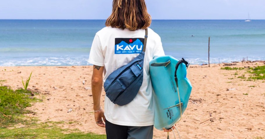 man wearing mini kavu sling bag and shirt holding a surf board