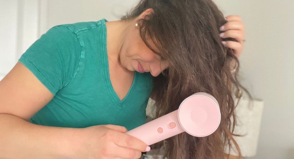 woman using pink blow dryer on hair