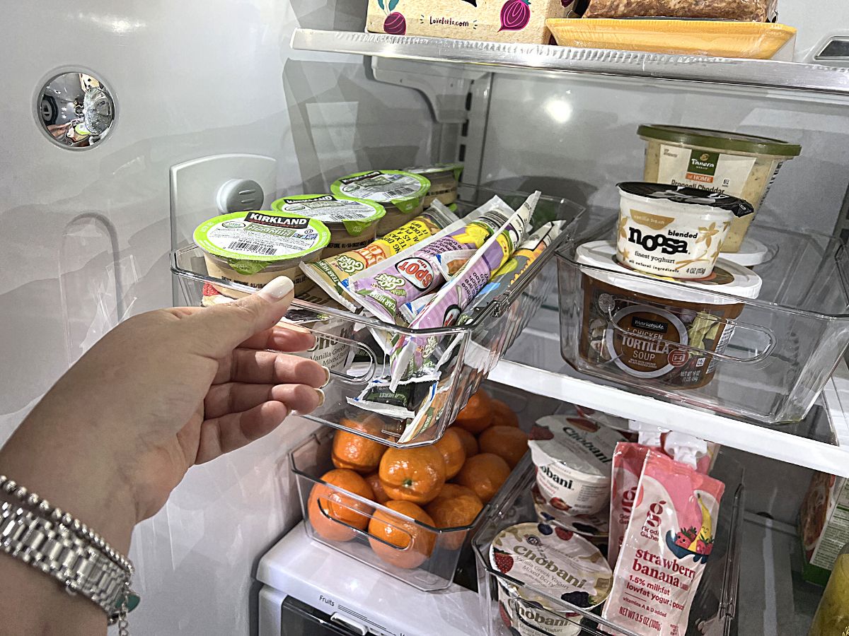 refrigerator organized with multiple clear bins holding snacks, yogurt, and oranges