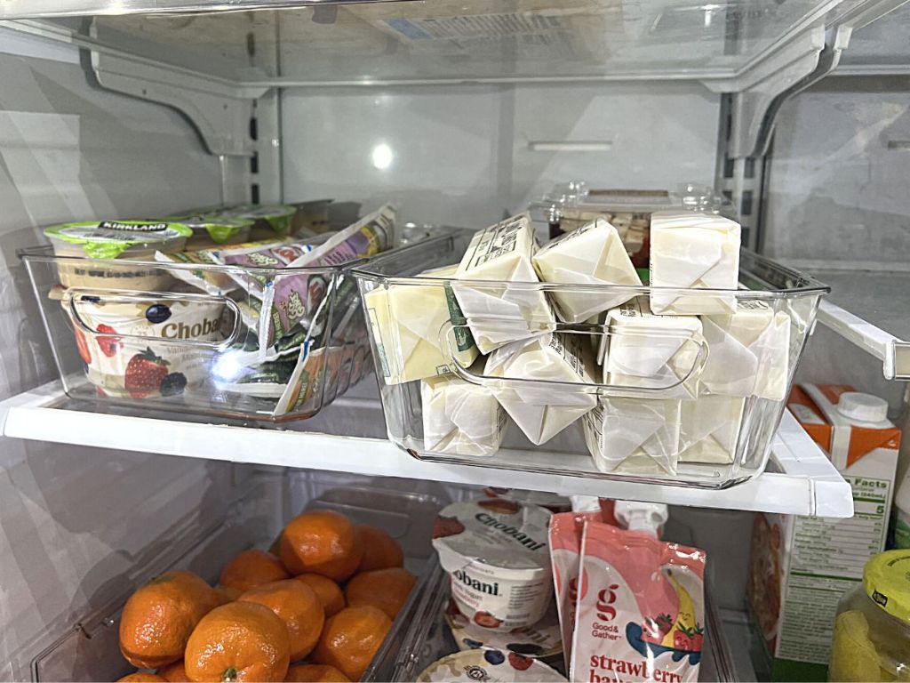 clear organizer bins in refrigerator holding yogurt, butter, and oranges 