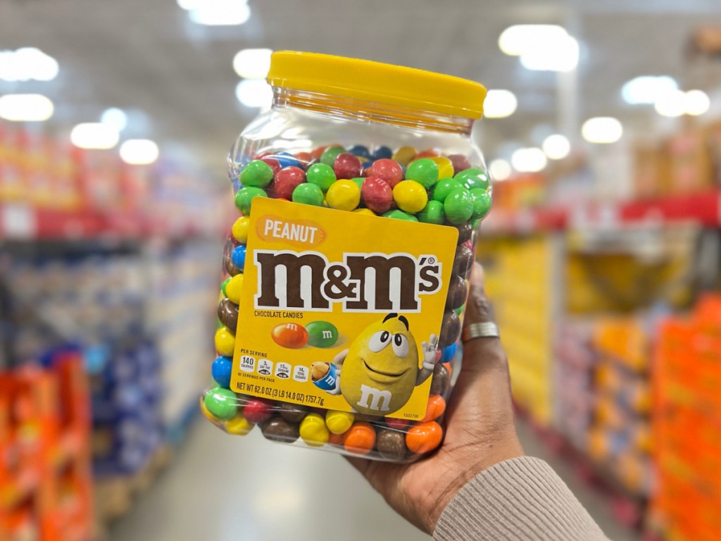 person holding up huge container of M&M's inside Sam's Club store