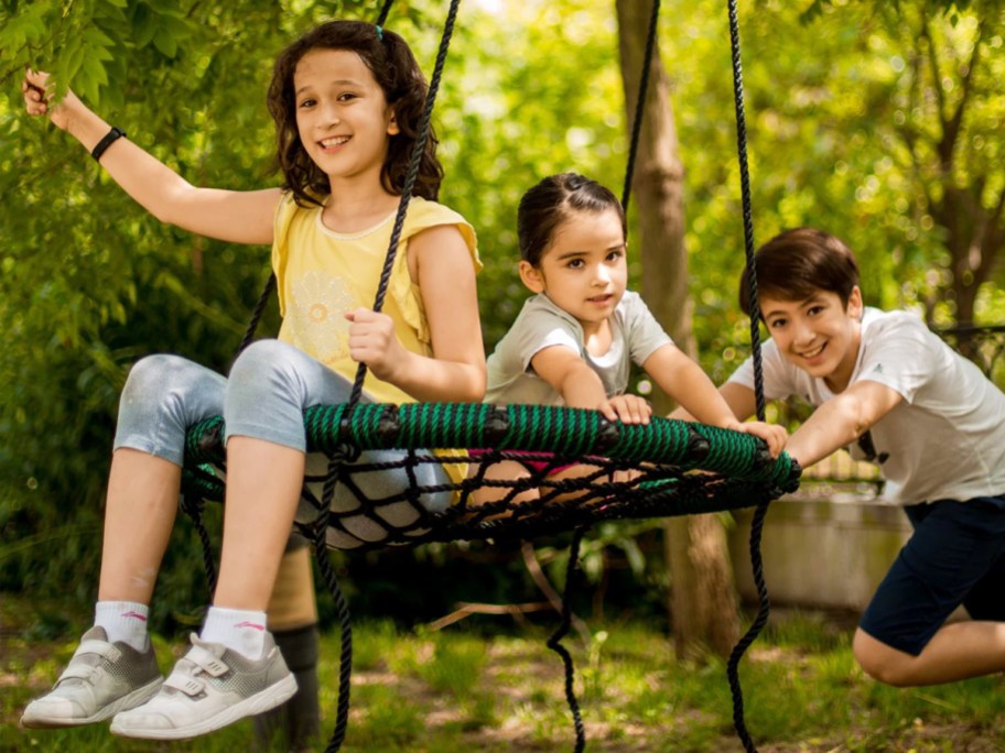 three kids playing on a green and black nest swing