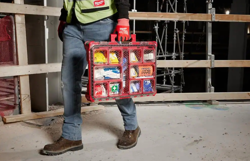 Person at a construction site carrying a Milwaukee First Aid kit case.