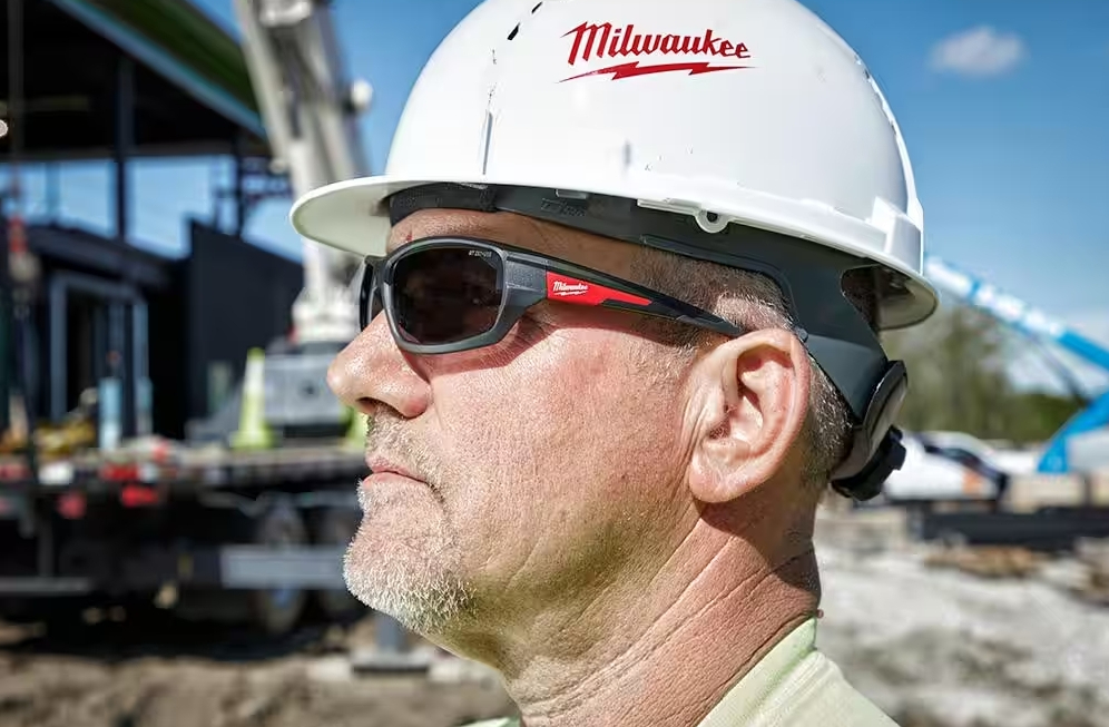 Man at a construction site wearing a hard hat and Milwaukee safety glasses.