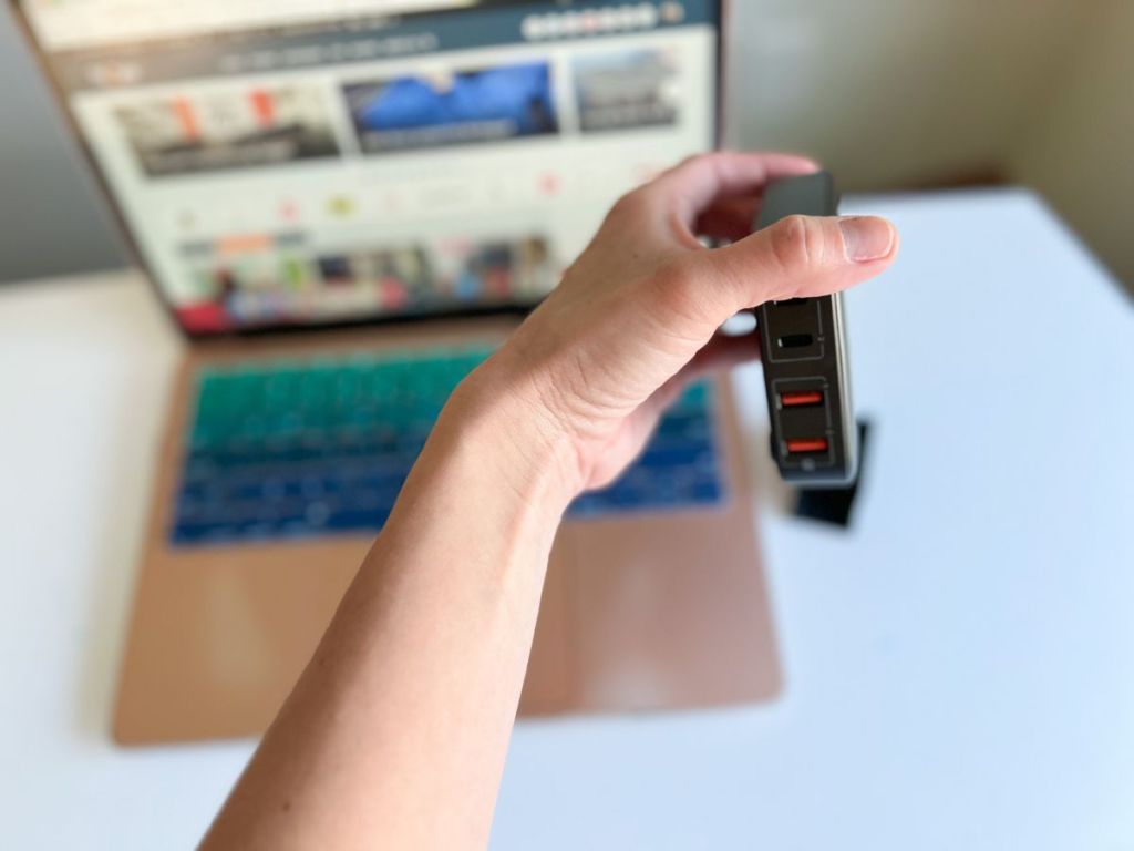 hand holding Momax USB C Charging Station with laptop in background