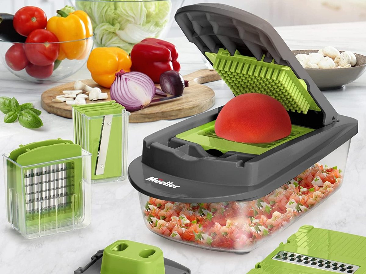 Grey and green kitchen slicer with attachments and vegetables around it