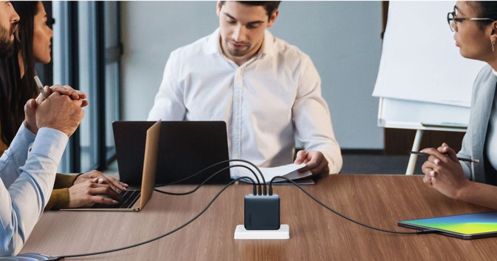 black 4-port charger with multiple devices plugged into it and people sitting around the table in a meeting