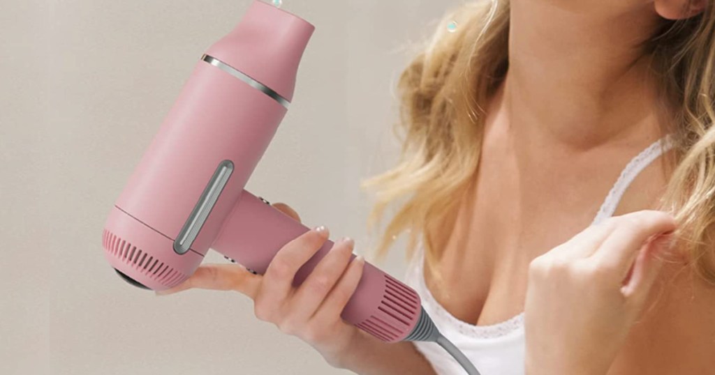woman drying her blonde hair with a pink colored hair dryer
