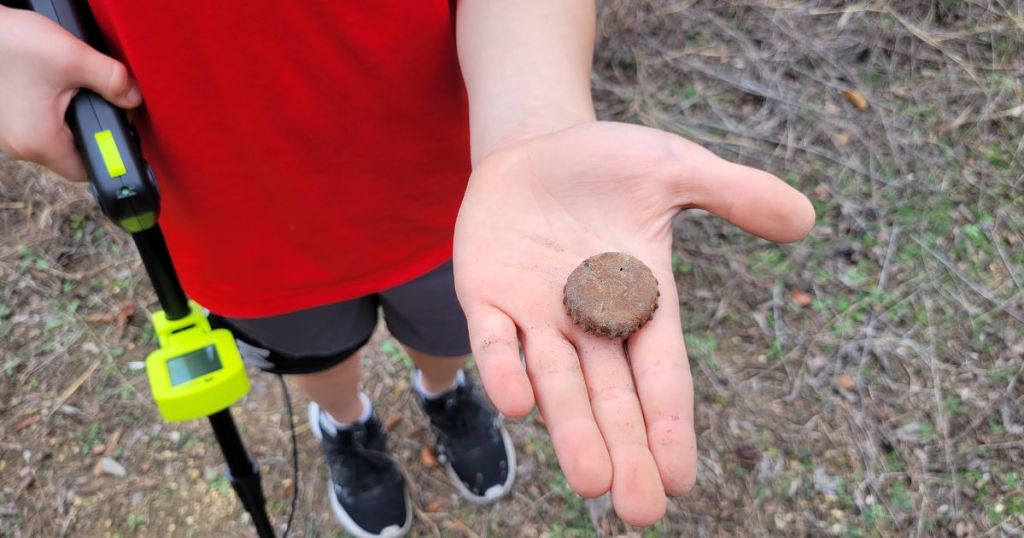 kid holding metal detector in one hand and dirty metal bottle cap in other