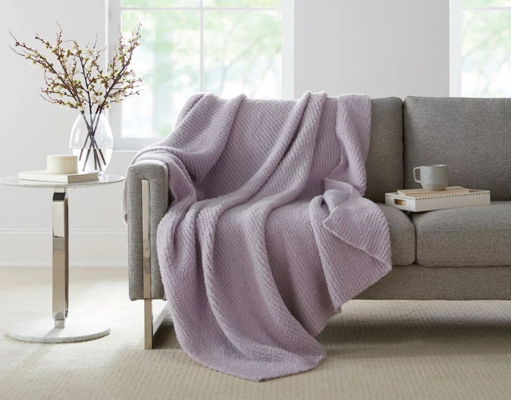 Purple throw blanket on a grey couch with a tray and a coffee mug next to it