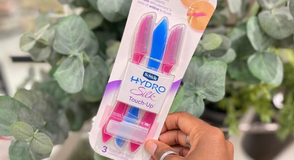 hand holding up a pack of 3 Schick Hydro Silk Dermaplaning Touch Up Razors in front of a fake plant