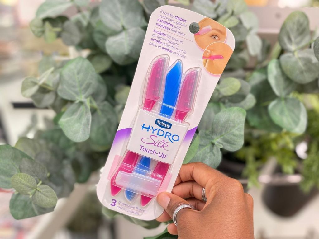 hand holding up a pack of 3 Schick Hydro Silk Dermaplaning Touch Up Razors in front of a fake plant