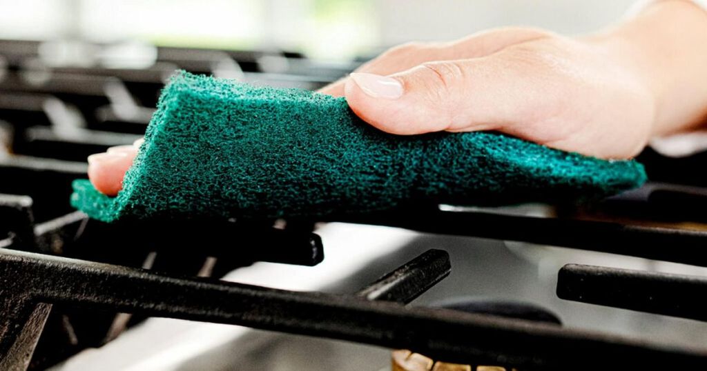 A hand cleaning a cast-iron grate with a scouring pad