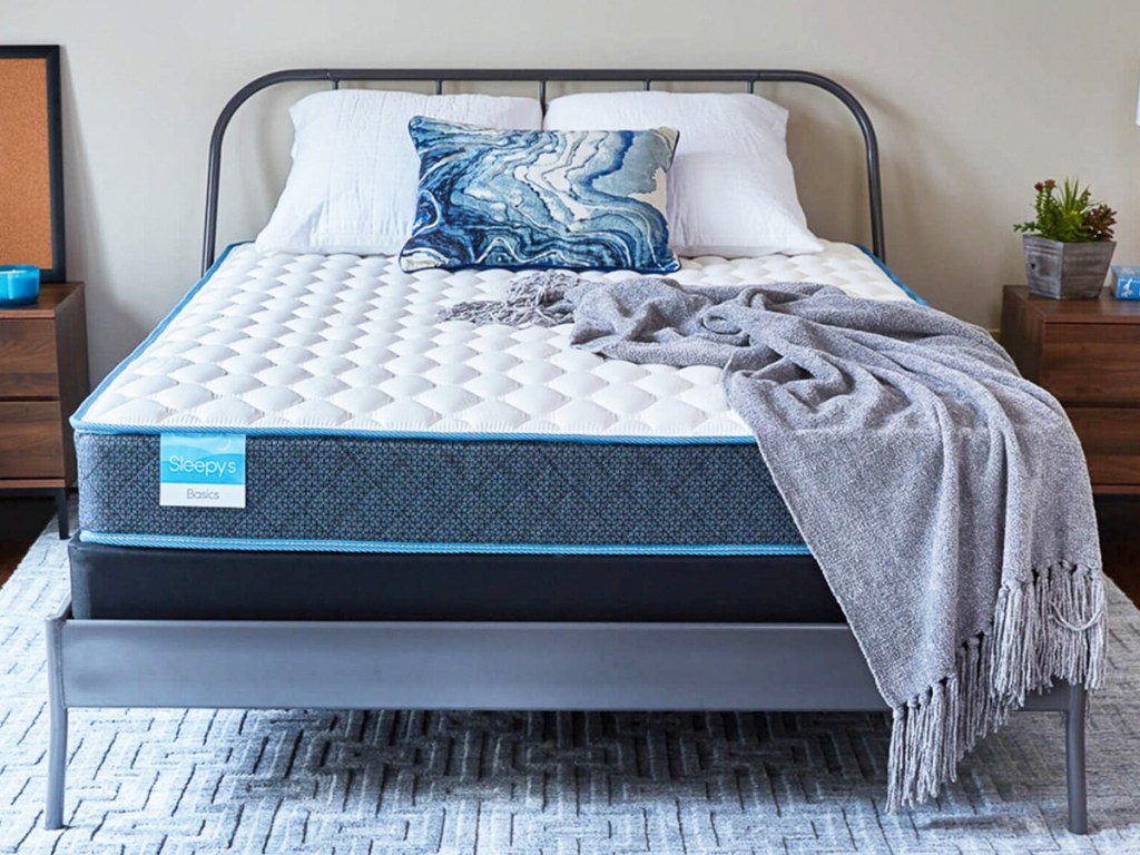 mattress on a metal bed frame with throw blanket on top