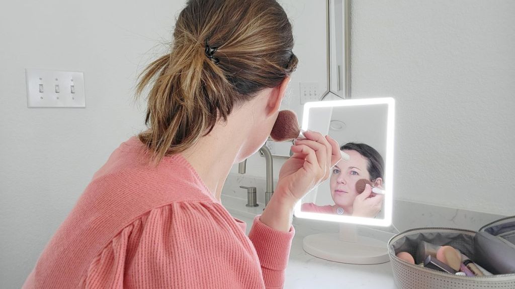 Woman putting on makeup in front of a lighted mirror