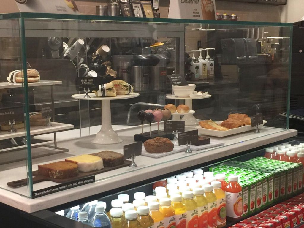 Starbucks bakery with breads, sandwiches, cake pops, brownies and an assortment of bottle and packaged drinks on the shelves below