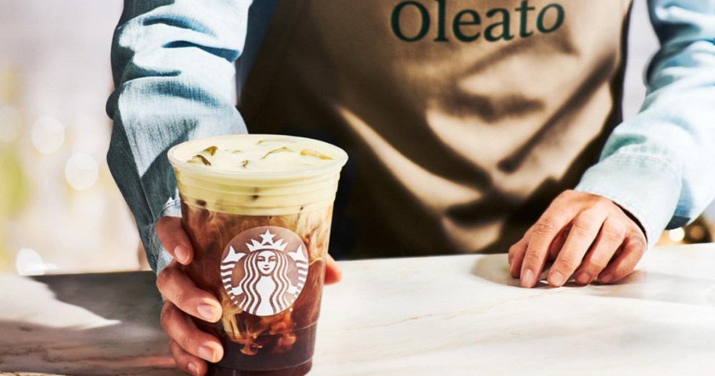 barista serving a Starbucks Oleato iced coffee and wearing a brown apron