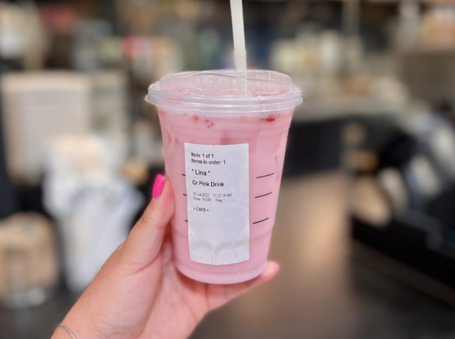Hand holding up a real Starbucks pink drink near the Starbucks counter