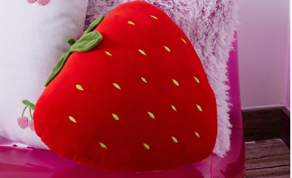 Strawberry-shaped plush throw pillow on a bed