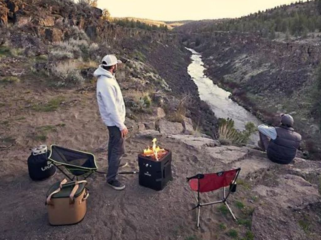 2 men camping with gear and firepit speaker on mountain