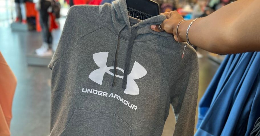 hand holding a hanger with a gray under armour fleece hoodie on it