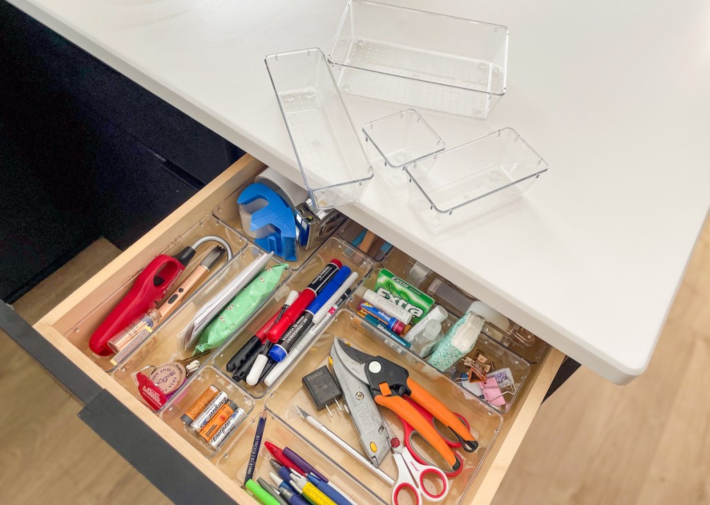 top view of organized junk drawer with clear acrylic containers on white countertop