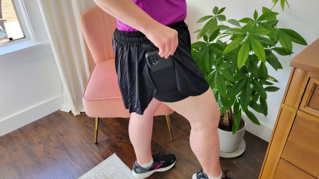 Woman putting a phone in the pocket of her running shorts