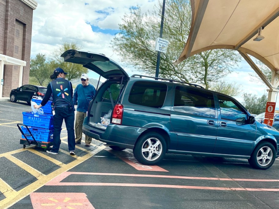 mini van pulled into walmart grocery parking spot while walmart employees load groceries into car