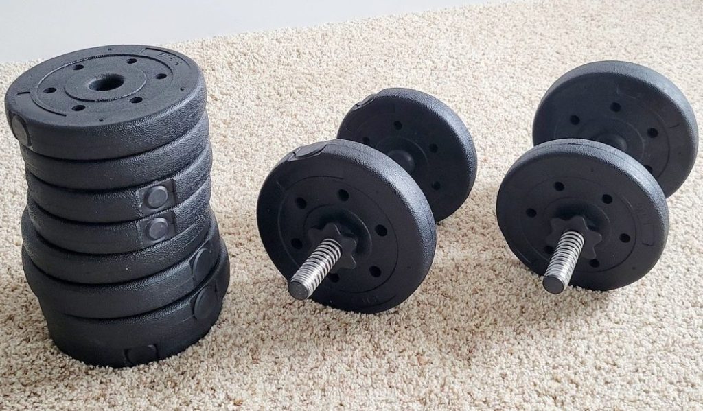 a stack of weight plates next two two heavy duty dumbells all set on a carpet