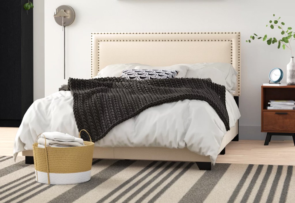 beige upholstered bed in bedroom with striped rug
