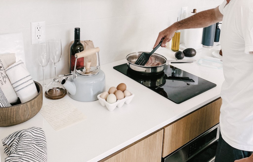 person cooking bacon on cooktop with half dozen farm fresh eggs