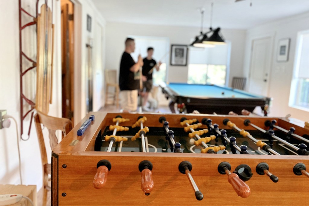 close up of foosball table with men in background playing pool