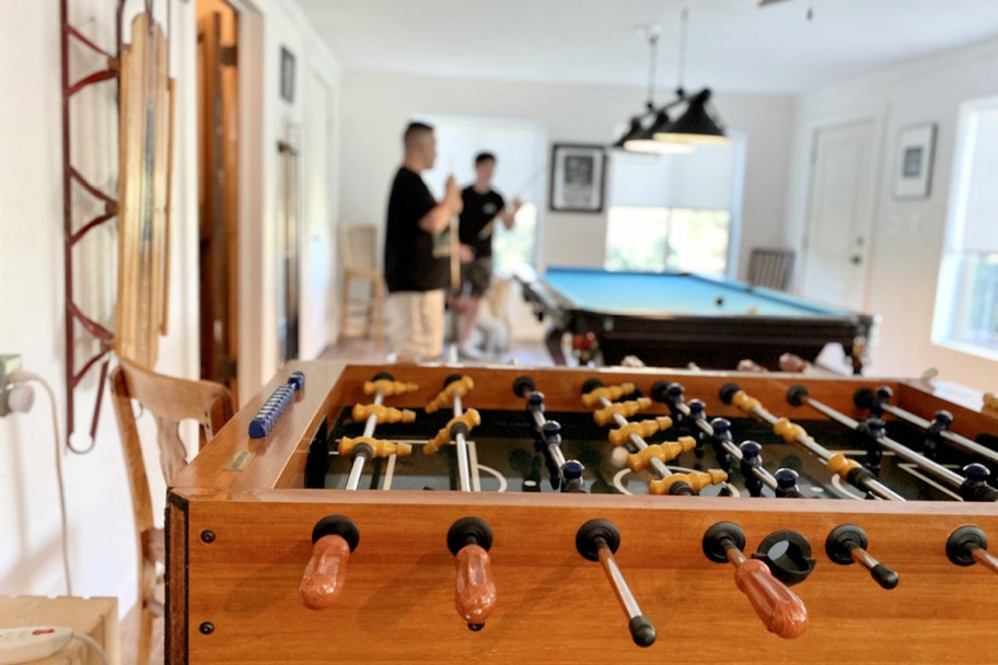 close up of foosball table with men in background playing pool