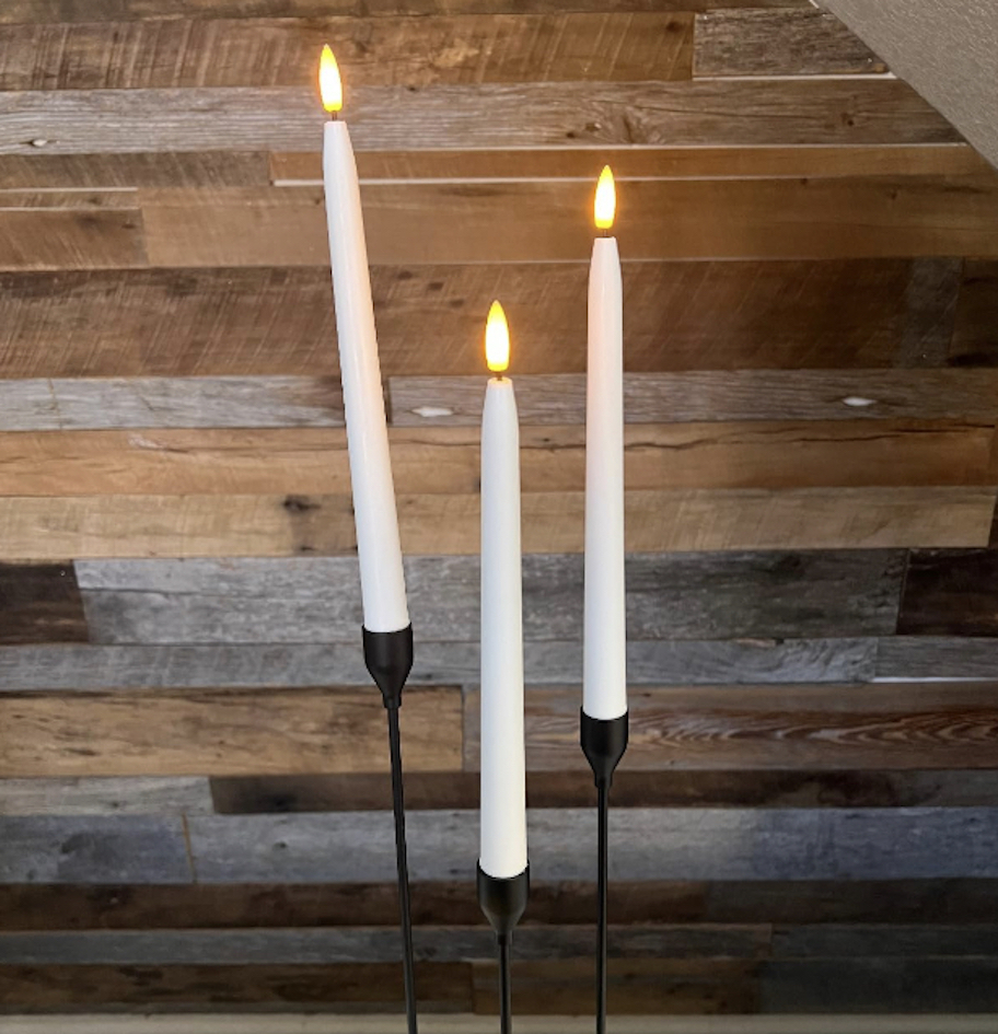 white flameless candles in black candle holders in front of wood wall